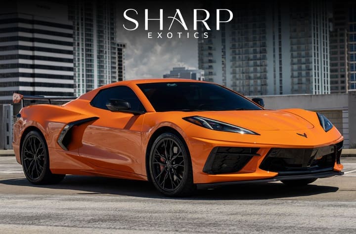Orange sports car parked on a rooftop with city buildings in the background, featuring the logo "Sharp Exotics" above.