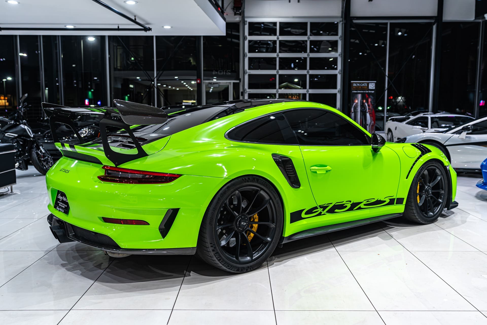 Porsche GT3 RS Bright green sports car with black accents and a large rear spoiler, parked indoors on a white tiled floor.