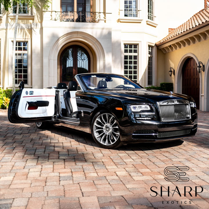 Black convertible luxury car with open doors parked on a brick driveway in front of an elegant house with arched entrance.