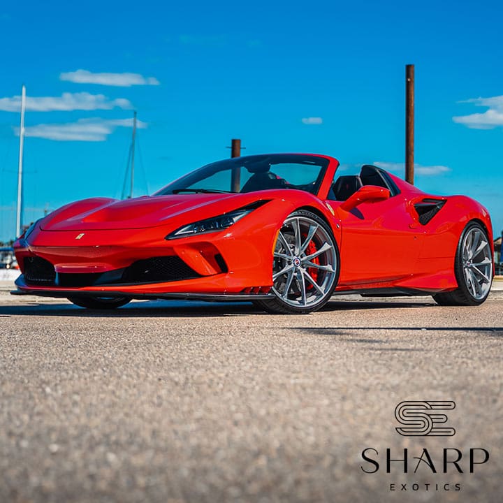 Red sports car with sleek design and convertible top parked on a sunny day, blue sky in the background, "Sharp Exotics" logo visible.