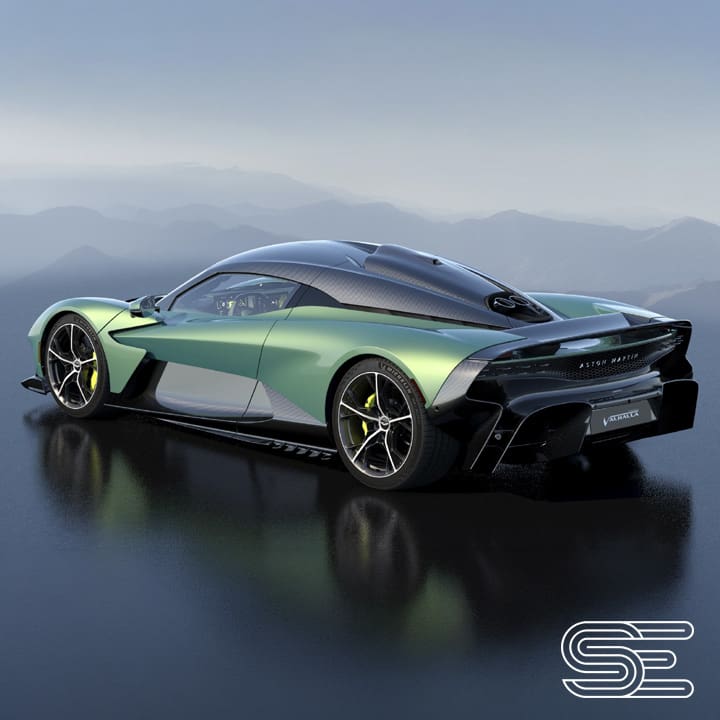 Aston Martin Valhalla (4) Sleek green sports car with aerodynamic design and black accents, parked on a reflective surface with mountains in the background.