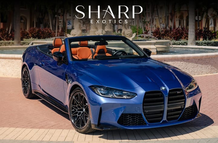 Blue convertible sports car with orange interior parked on a circular driveway, surrounded by palm trees and a fountain.