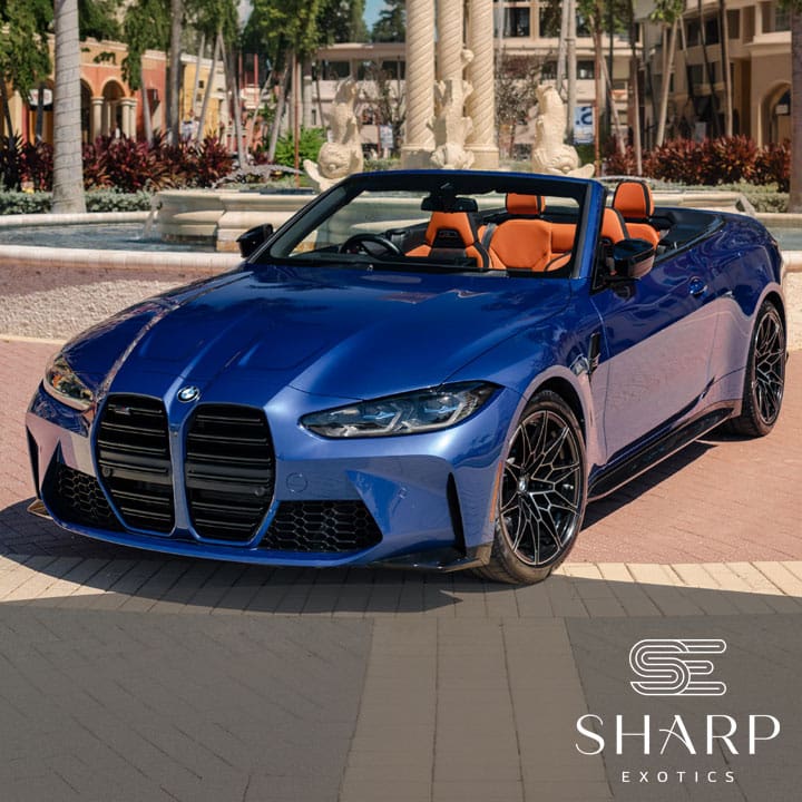 Blue convertible sports car with orange interior parked in front of a fountain, surrounded by palm trees and buildings.
