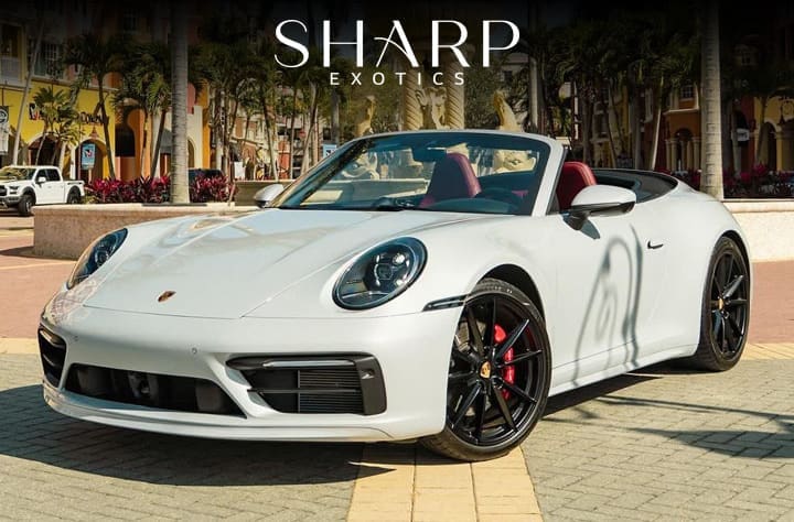 White convertible sports car with red interior parked on a sunny street, surrounded by palm trees and colorful buildings.