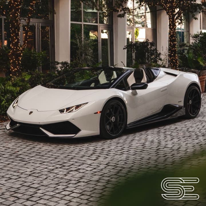 White convertible sports car parked on a cobblestone driveway, surrounded by greenery and string lights.