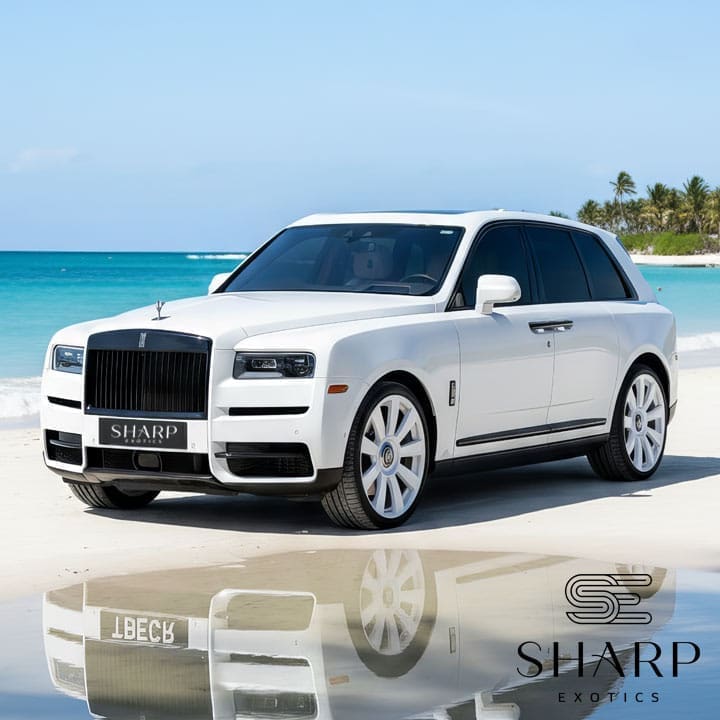 White luxury SUV parked on a beach with clear blue water and palm trees in the background, featuring "Sharp Exotics" branding.