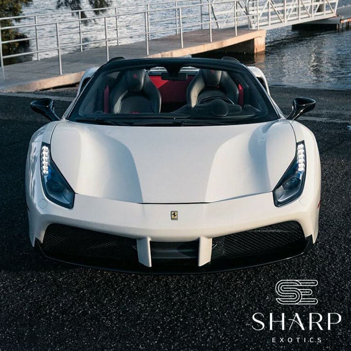 White convertible sports car parked near a waterfront with a dock in the background, logo "Sharp Exotics" in the corner.