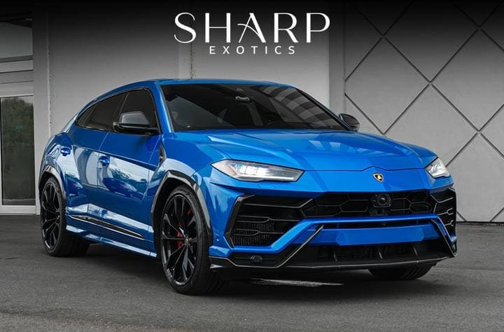 Blue luxury SUV with black rims parked in front of a geometric wall, featuring the logo "Sharp Exotics" above.