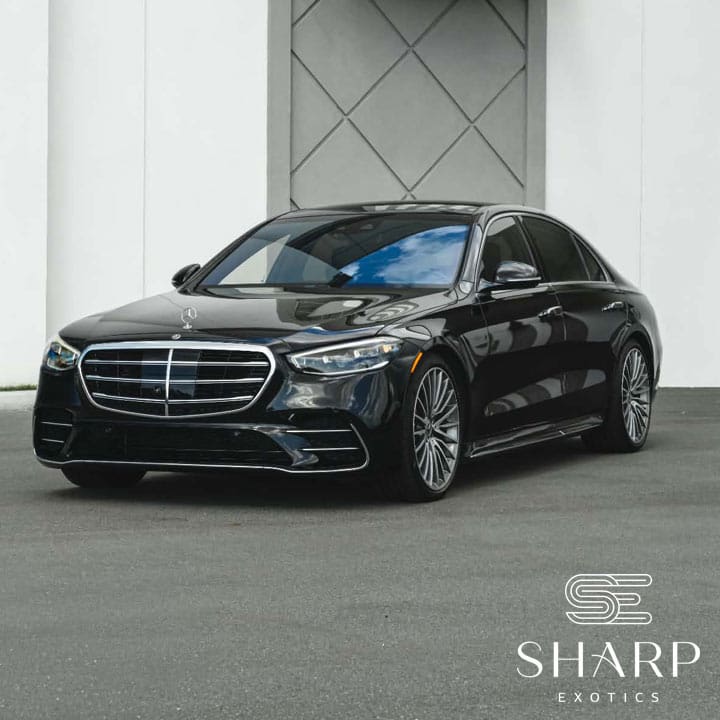 Mercedes s580 Black luxury sedan parked in front of a geometric-patterned wall, featuring a prominent grille and sleek design. Logo reads "Sharp Exotics